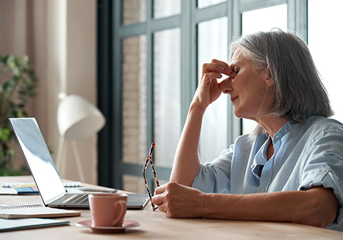 Tired elderly woman taking off her glasses suffering from burnout.